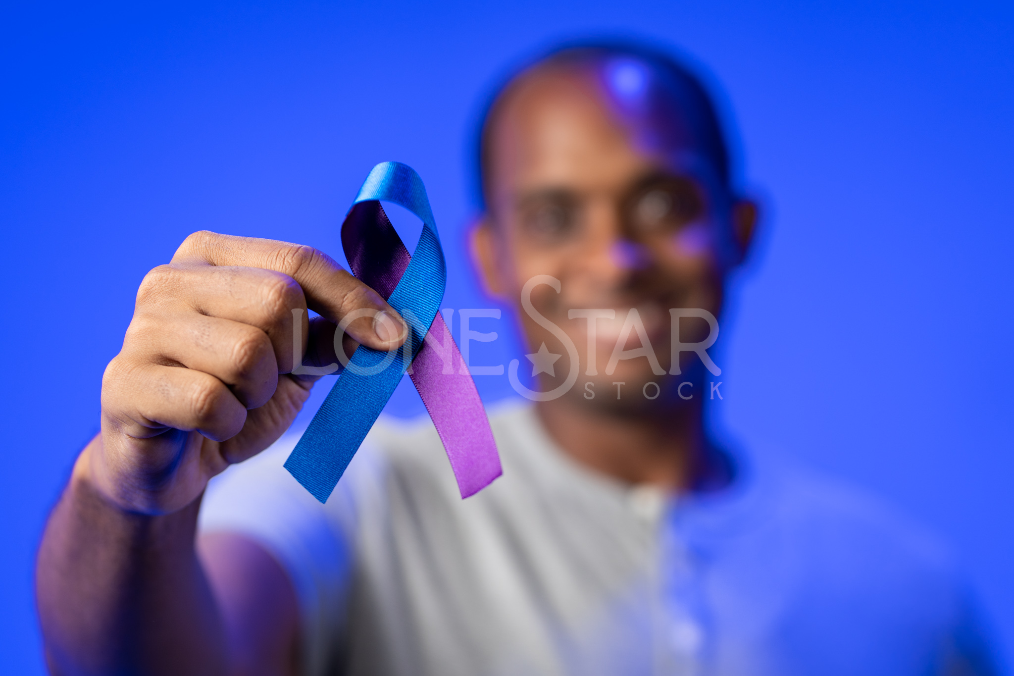 Preview of a Smiling man holding up a Suicide Prevention Awareness Ribbon up to the camera with a blue background