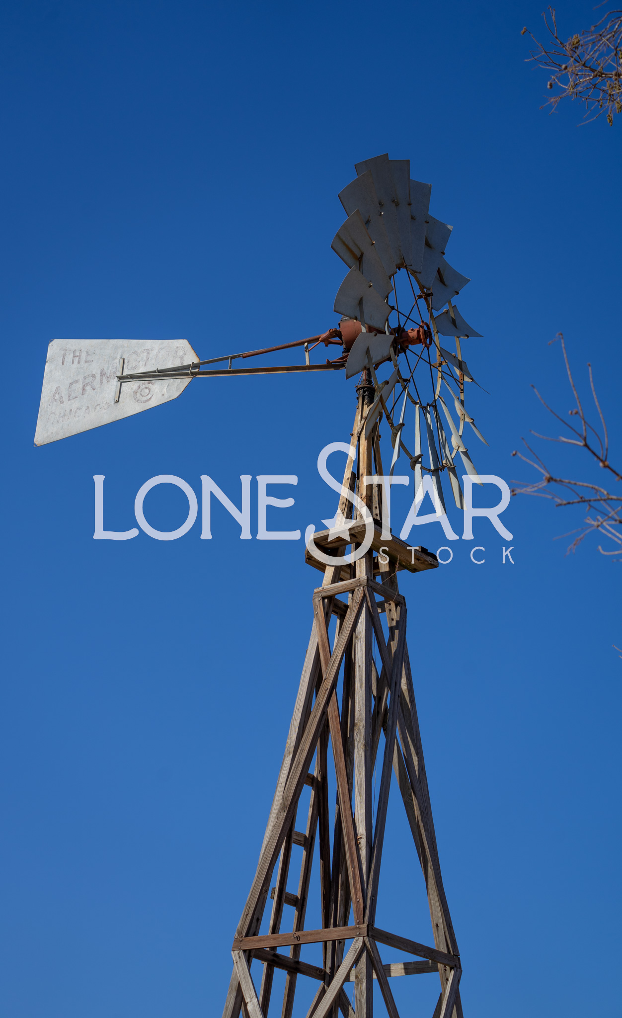Preview of Old Metal Aeromotor Wind Mill on Grapevine's Main Street with Branches and Blue Sky in Background